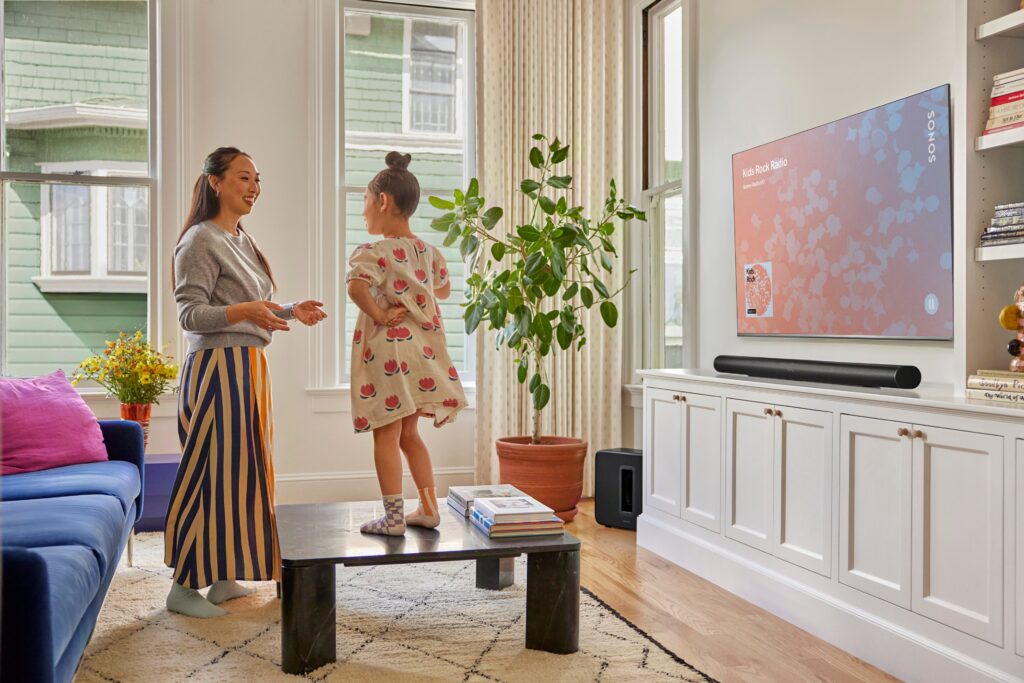 Die Sonos Arc Ultra Soundbar in der schwarzen Ausführung. Der Sonos Sub 4 versteckt sich in der Ecke.